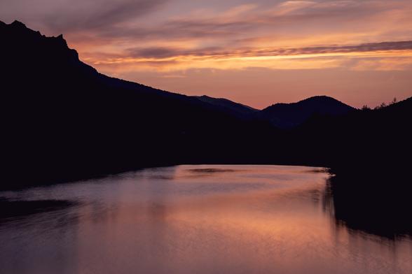 Silhouettes of mountains and a reservoir with orange twilight lights