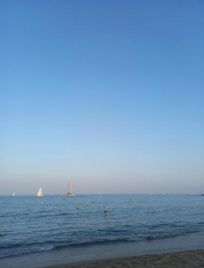 Playa, el mar al atardecer con un barco blanco en la línea del horizonte.