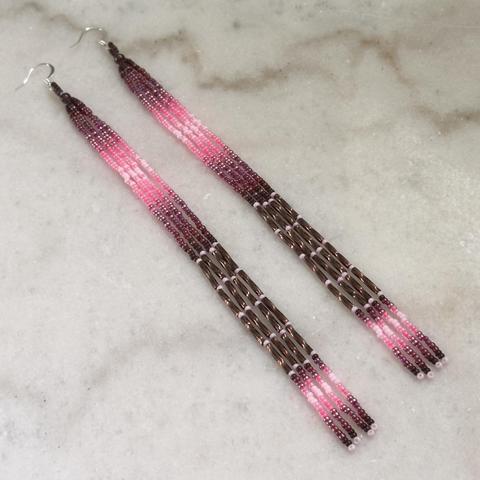 A pair of long beaded dangle earrings in shades of pink and brown against a white marble background