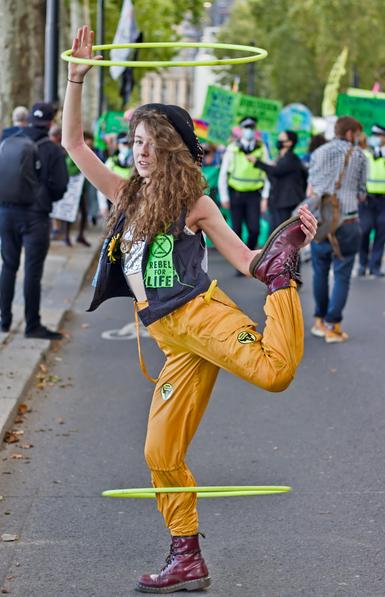 A young XR protester in the street is spinning hula hoops with her arms and legs