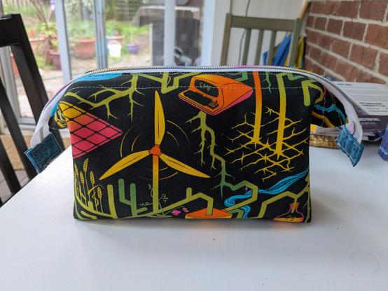 Zippered bag in a black fabric with green, blue, orange, yellow, on a black background.