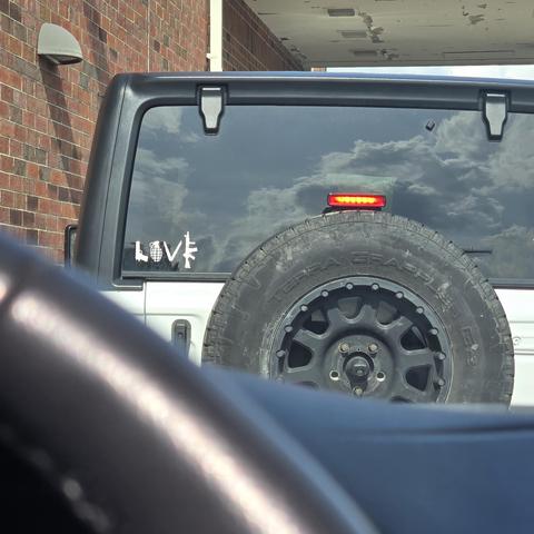 A white jeep with a window cling that says love but it is formed by guns