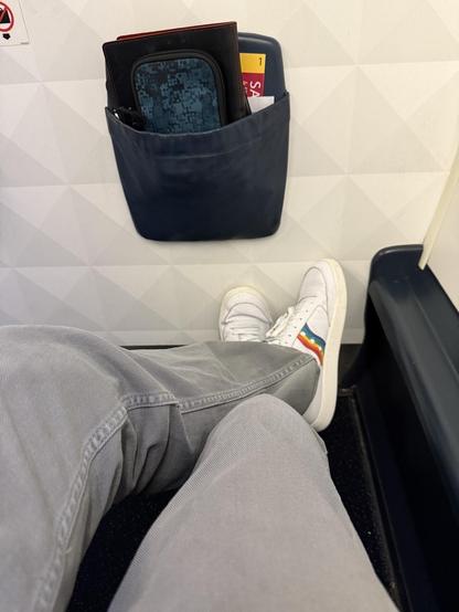 Legs extended while seated on plane, sporting white sneakers with six color stripes