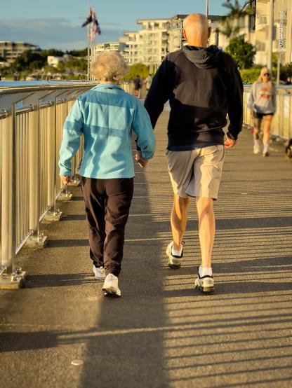 Early morning walkers on the riverwalk. A *mature* couple are striding away from the photographer, hand-in-hand.