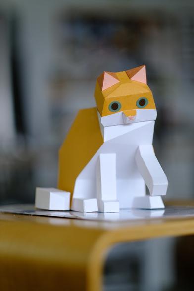 photo of an assembled paper orange cat. It looks like it’s about to knock something off the table with its paw
