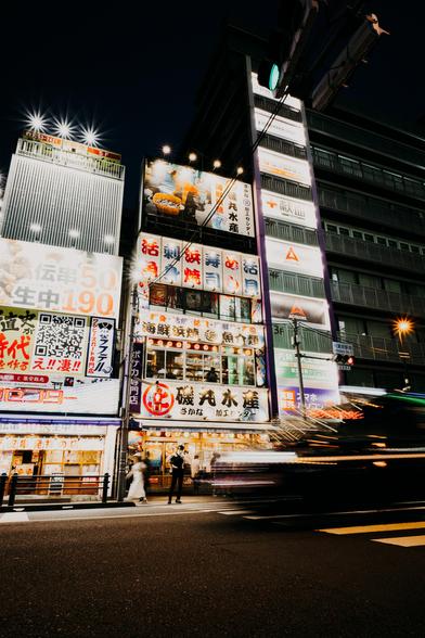 photo of a busy street with a building full of advertisement billboards and neon signs, glowing bright in the dark night
