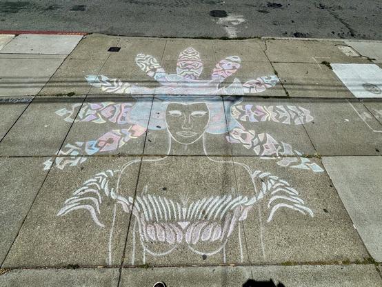 A chalk drawing on the sidewalk of a woman with large feathers in her hair. The colors are pastel and their are several intricate and symmetrical patterns to the feathers and other parts of the drawing. The drawing i avoubt 4 feet tall and 5 feet wide.