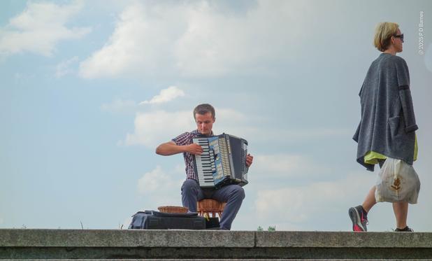 A busker plying his trade on the Vistula river riverwalk. A pedestrian is walking by unmoved. Mind you, he is playing a piano-accordion.