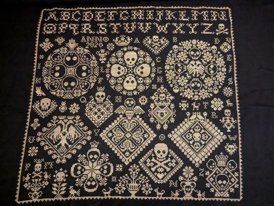 photo of a cross stitch sampler using white floss on black linen. the pattern features a variety of elaborate motifs and a lot of skulls.

pattern: all souls vierlanden by ben drew