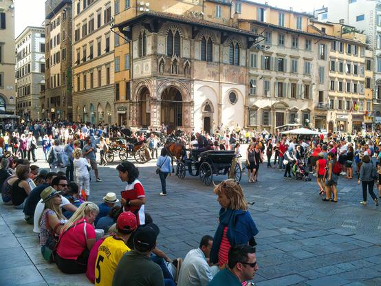 A crowded and hectic scene in the Piazza del Duomo, Florence. The steps are packed with seated, weary tourists and the square is thronged with horse-carriages, street vendors, performers and everywhere tourists. It's a sunny day, but obviously not hot.