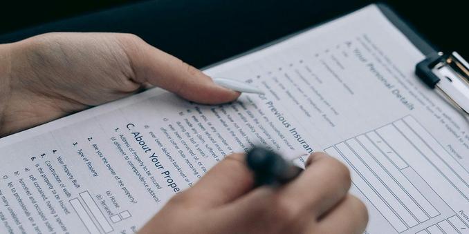 Two feminine hands, one holding a pen, filled out a form on clipboard.