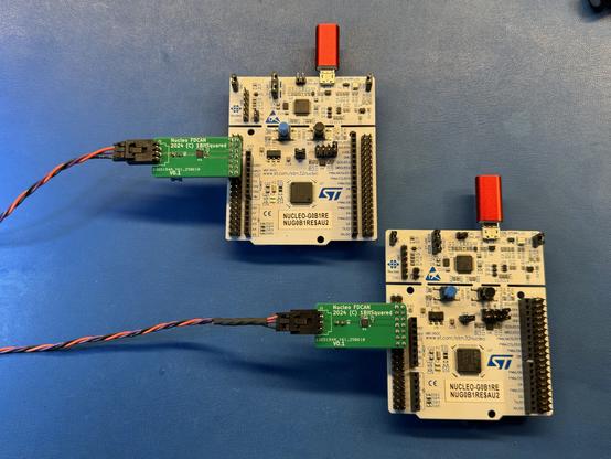 Two STM32G0B1 dev boards with small green adapter boards plugged in and twisted cables connected. The boards also have small red micro USB to USB-C adapters plugged into the stlink programming port.