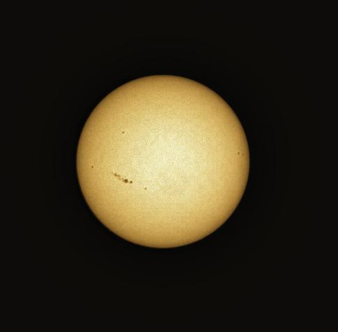 The sun against a black background. There is a prominent band of sunspots in the lower left quadrant, and other scattered smaller sunspots.
