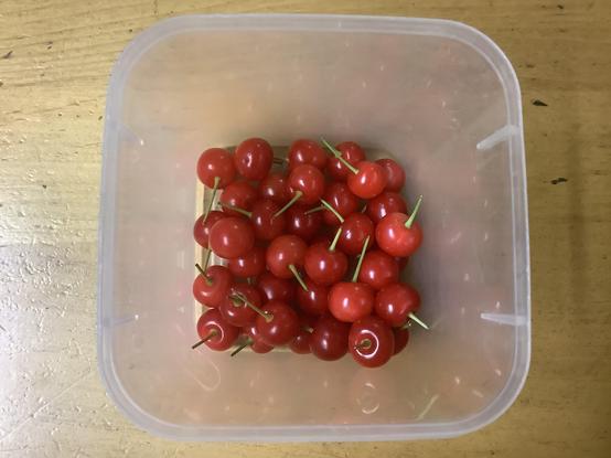 A bunch of beautitul, bright red tart cherries in a clear plastic container.