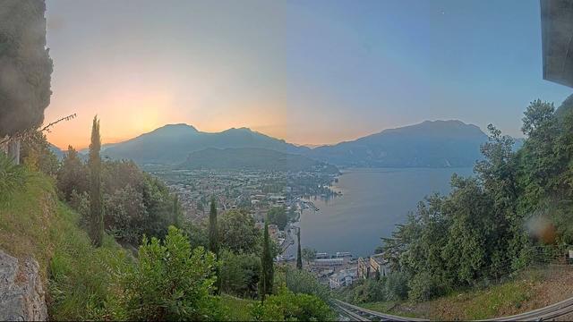 Sonnenaufgang mit Bergen und See. Stadt am Ufer. Vorne Grün.