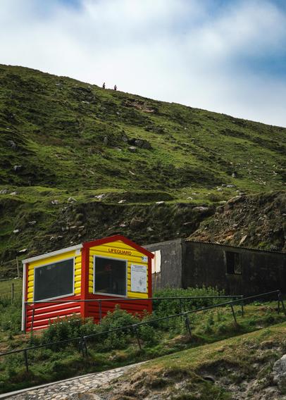 a lifeguard station at the base a mountain with two hikers descending it