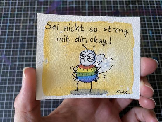 Die Pupsbiene (eine Regenbogenbiene) die streng guckt. Darüber der Text: "Sei nicht so streng mit dir, okay!"