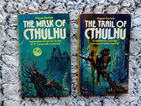 Two books sat on a furry blanket.

Both vintage paperbacks, both with lurid covers.

The one on the left is Mask of Cthulhu, a collection of stories  by August Derleth. The one on the right is Trail of Cthulhu, a collection of stories by August Derleth.