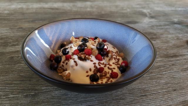 Eine blaugraue Schüssel mit Müsli, Joghurt und frischen Beeren steht auf einem verwitterten Holztisch