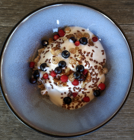 Eine blaugraue Schüssel mit Müsli, Joghurt und frischen Beeren steht auf einem verwitterten Holztisch