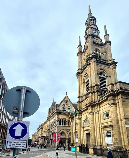 A view along the Georgian and Victorian buildings on Buchanan Street in Glasgow. In the foreground is a sign with an arrow pointing upwards which says Don't forget to look up and appreciate the architecture.