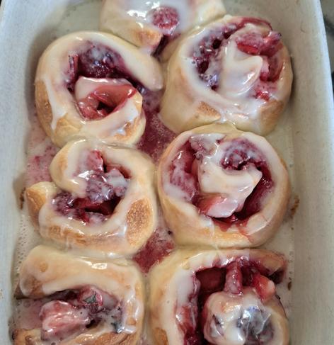 A rectangular white ceramic baking dish with strawberry and raspberry sourdough rolls. The fruit is from my garden. The rolls are snuggled together, the red fruits bursting from the top of the rolls. The sourdough of the rolls is a golden colour.