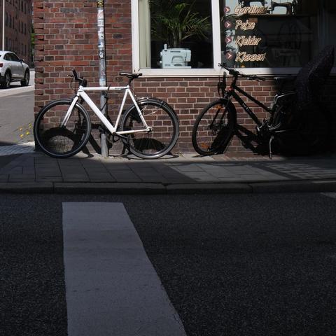 Ein weißes Fixy oder Singlespeed von Bonvelo steht in der Mittagsonne vorn einer Backsteinwand