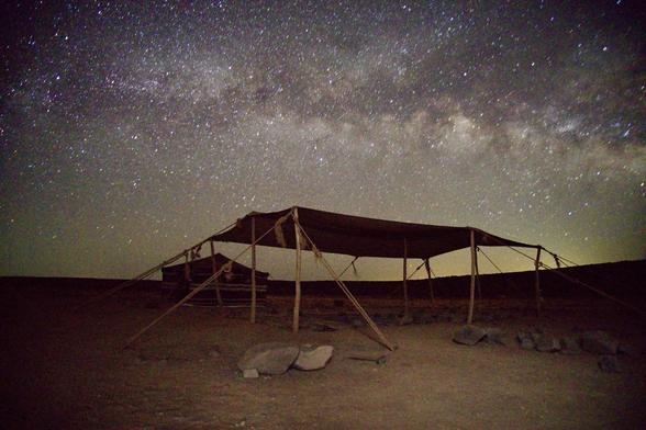 A Bedouin style shade tent in the foreground with the Milky Way in the background.