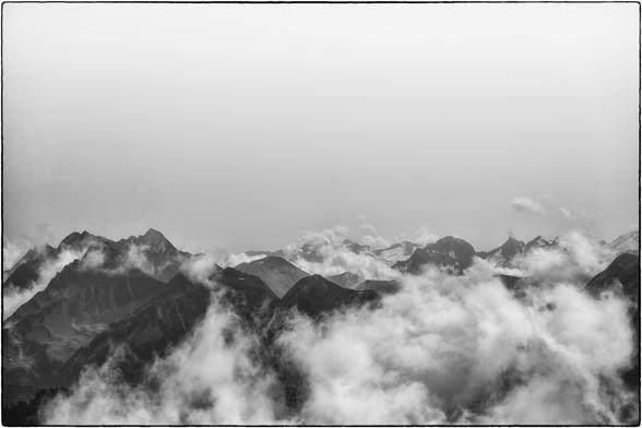 Schwarzweissfotografie einer Gebirgslandschaft mit Nebelschwaden in den Tälern.