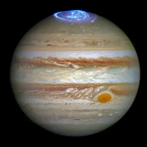 Die runde Jupiterscheibe füllt fast das gesamte Bild aus, nur die freien Ecken sind schwarz. Auf der Oberfläche des Planeten sind horizonal vielfarbige Wolkenbänder zu sehen, die gelblich, weiß, orange oder rötlich und selten blassblau erscheinen. Die Bänder sind in sich verwirbelt und teilweise mit Flecken durchsetzt. Einer dieser Wirbel ist besonders groß und auffällig orangerot. Er befindet sich in der unteren rechten Seite der Scheibe und wird begleitet von einem ausgerägten Wirbelfeld direkt links davon. Oben in der Mitte wickeln sich grell blau-weiß leuchtende Spuren mehrfach um den Pol herum.
