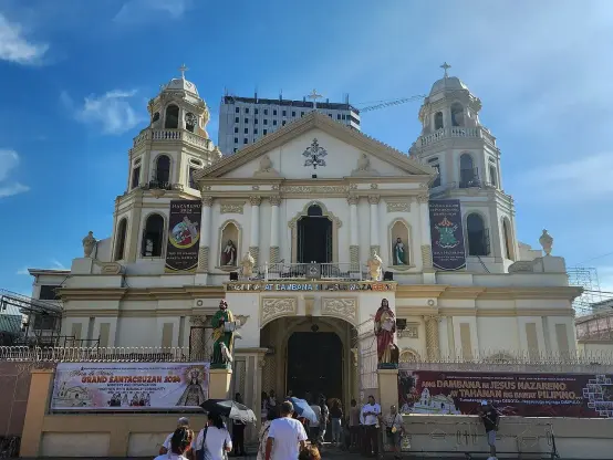 The image shows a large church or basilica with impressive architecture. It features two prominent towers and ornate decorations on the facade. The building appears to be well-maintained, with banners hanging on the exterior. There are people in front of the church, suggesting it may be a place of worship or a tourist attraction. The overall setting seems to be a bright day, with clear blue skies.

Image Credits: Wikimedia / LMP 2001 / CC BY-SA 4.0