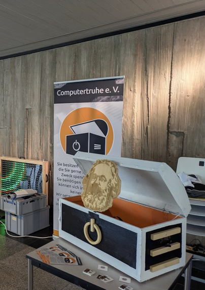 Bild zeigt Stand der Computertruhe Chemnitz mit Banner und der echten Holztruhe mit Marx-Kopf sowie Flyer und Sticker.