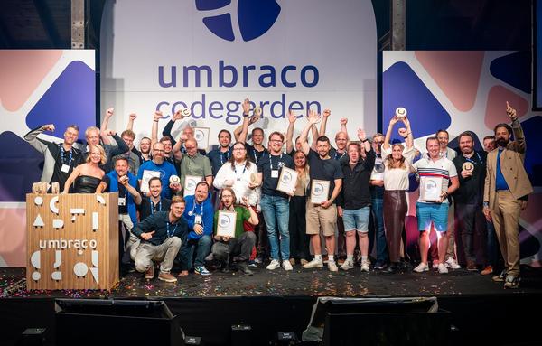 A large, jubilant group of award winners and presenters pose together on stage at Codegarden. Many hold up wooden Umbraco trophies and framed certificates, raising their fists in celebration. The backdrop features the Umbraco and Codegarden logos, with confetti scattered across the stage floor, capturing the excitement and energy of the moment.
