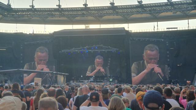 Foto. Bruce Springsteen steht im Frankfurter Waldstadion auf der Bühne und spielt Mundharmonika. Weil ich ziemlich weit hinten stand, ist der Boss nur sehr winzig zu sehen, über der Bühne sind aber drei riesige Bildschirme, auf denen er auch in groß zu sehen ist. Vor der Bühne jede Menge Leute.