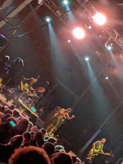 Chatpile on stage at PrimaveraSound Porto. Looks like a generic pic of a small festival stage. The framing is off kilter, some bright spotlights look nice beaming cones of light over the heads of the band. 
The singer is wearing only shorts and looks like actor Rob Delaney but less hairy. He is mid song.