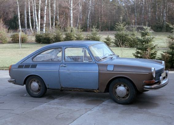 Ein Foto eines VW 1600 TL in blauer Lackierung mit zwei braun lackierten, vorderen Kotflügeln.  Der Wagen steht auf einem Betonuntergrund am Rand einer Rasenfläche die von kleinen Fichten und in der Ferne von hohen, laublosen Birken gesäumt ist. 
Das Bild ist etwas Februar 1984 aufgenommen worden und wurde vor kurzem von dem Diapositiv eingescannt.