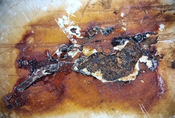extreme nahaufnahme eines rostflecks in eigentlich weiß lackiertem stahl. der lack ist hier allerdings beschädigt, zerkratzt und teilweise abgeplatzt. an der abgeplatzten stelle schaut schwarz-braun meliert die inzwischen rauhe stahloberfläche hervor. drum herum sieht man, wie der rost sich schon unter dem lack ausbreitet, er erzeugt neben den scharf gezackten schmalen weißen rändern wo der lack abreißt einen unscharf begrenzten fleck, einen hof um die offene stelle, in schönen unterschiedlich hellen rost-orange-braunen tönen. alles in allem reine form, abstrakt aber natürlich gewachsen.