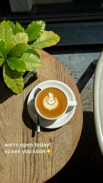 A Flat White with latte art on our wooden coffee table. Next to it a coffee plant
