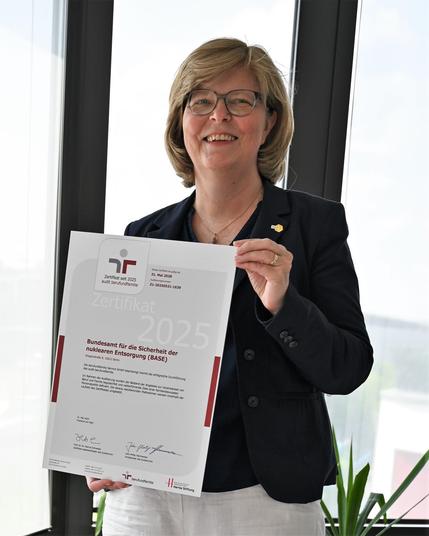 Person hält eine Zertifikatsurkunde für das Bundesamt für die Sicherheit der nuklearen Entsorgung (BASE) mit Gültigkeit bis 2028 hoch.