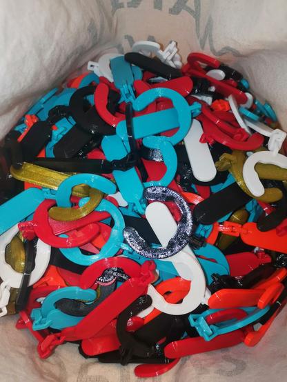 Inhalt eines Jutebeutels. Farbige (Weiß, Gold, Rot, Schwarz, Orange, Blau) Plastik-Clips an welchen eine Fläche hängt welche beschriftet werden kann.