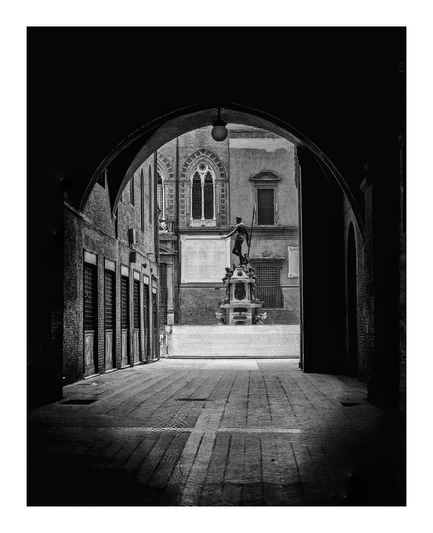 This is a black-and-white photograph showing a dark arched passageway leading outside to a square (Piazza del Nettuno). At the center of the photo, framed by the arch, is a classical statue of a man holding a spear, mounted on an ornate pedestal. The surrounding architecture is largely medieval, with arched windows, brick walls, and a cobbled/tiled floors. There is a strong contrast between the dark and shadowy archway and the brightly lit square outside.