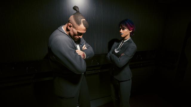 Cyberpunk 2077 screenshot player character and Jackie in suits in a dark room, arms crossed and looking serious.