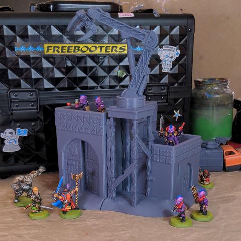 A grey plastic model of an adobe style workshop with a big grabby arm on top and several brightly colour models place around it all sitting on a messy desk.