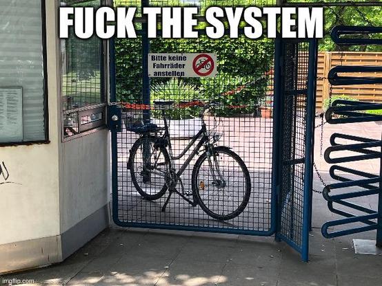 A bike parked behind a sign where it is said "Bitte keine Fahrräder anstellen" (please don't park bikes here). On the upper side on the picture, this is written"FUCK THE SYSTEM".