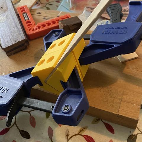 A small right angle in modelling plywood and veneer in a pair of big yellow and blue right angle clamps. A set square and some blocks are also in the picture. It is taken close up so the scale is confusing. The light casts shadows left to right.