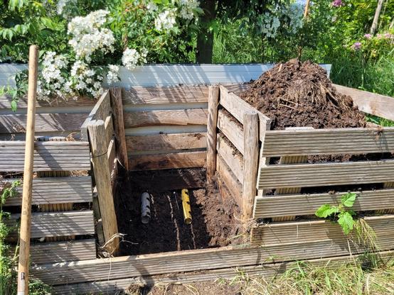 3bay compost system with the middel bay empty. On the bottom you see a grey and yellow pvc pipe with holes in them. They go through the back of the wooden structure to add a bit of airflow to the bottom of the pile
