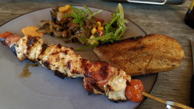 Tellerbild der marinierten Hähnchenspieße mit speckumwickeltem Grillkäse, Antipasti, Knoblauchbaguette und gemischtem Salat