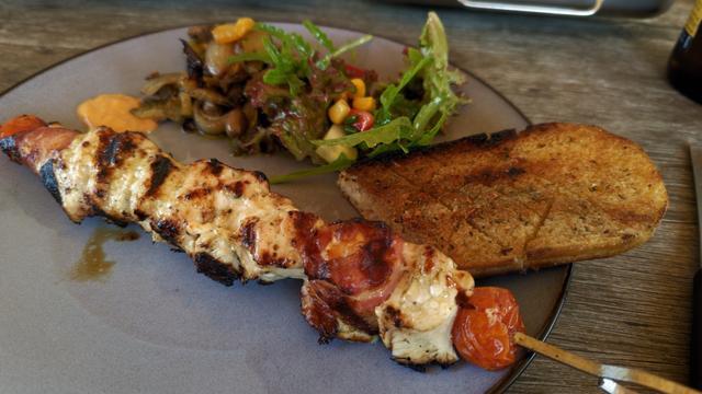 Tellerbild der marinierten Hähnchenspieße mit speckumwickeltem Grillkäse, Antipasti, Knoblauchbaguette und gemischtem Salat