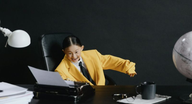 Image of little girl in oversized yellow suit playing with typewriter. Image by Cottonbro Studio via Pexels