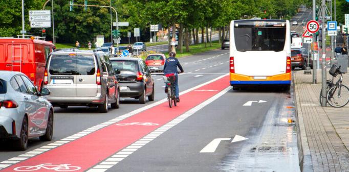 Eine Person radelt auf einem Radstreifen in Mittellage (RIM). Links von ihr sind diverse Geradeausspuren für den Kfz-Verkehr, rechts von ihr ist eine Rechtsabbiegespur mit einem Bus.